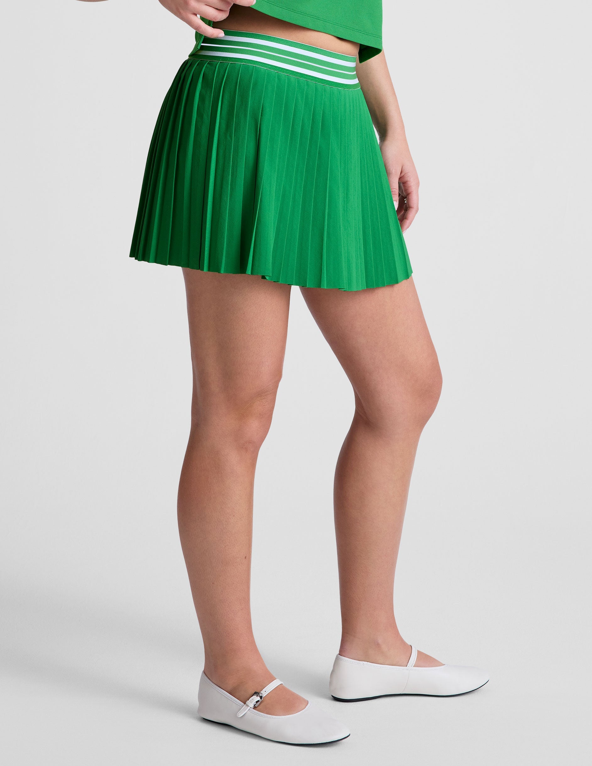 green pleated mini skirt with an exposed stripped elastic waistband​ and internal performance shorts with pockets​.