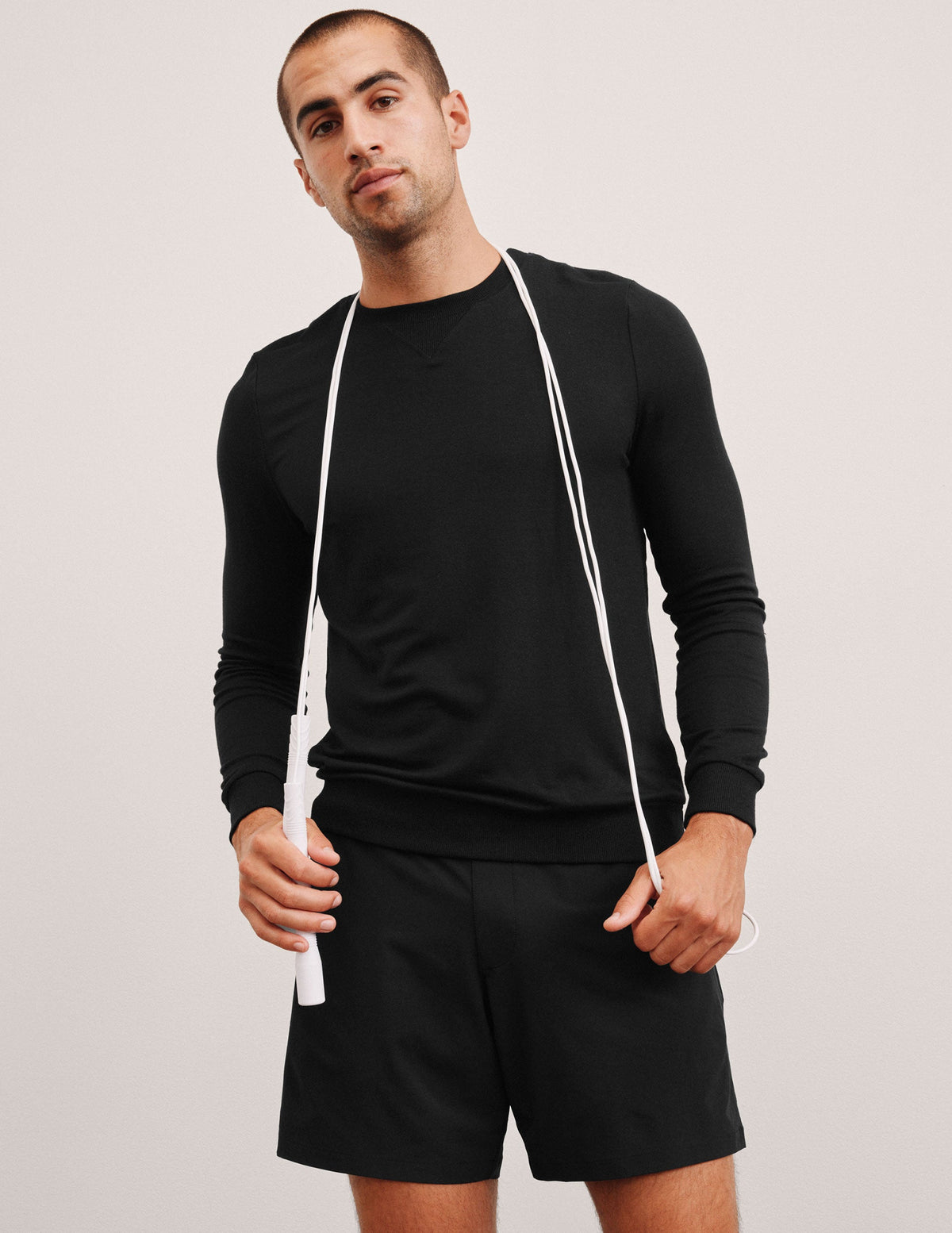 man wearing a black long-sleeve shirt and shorts on a light gray background.