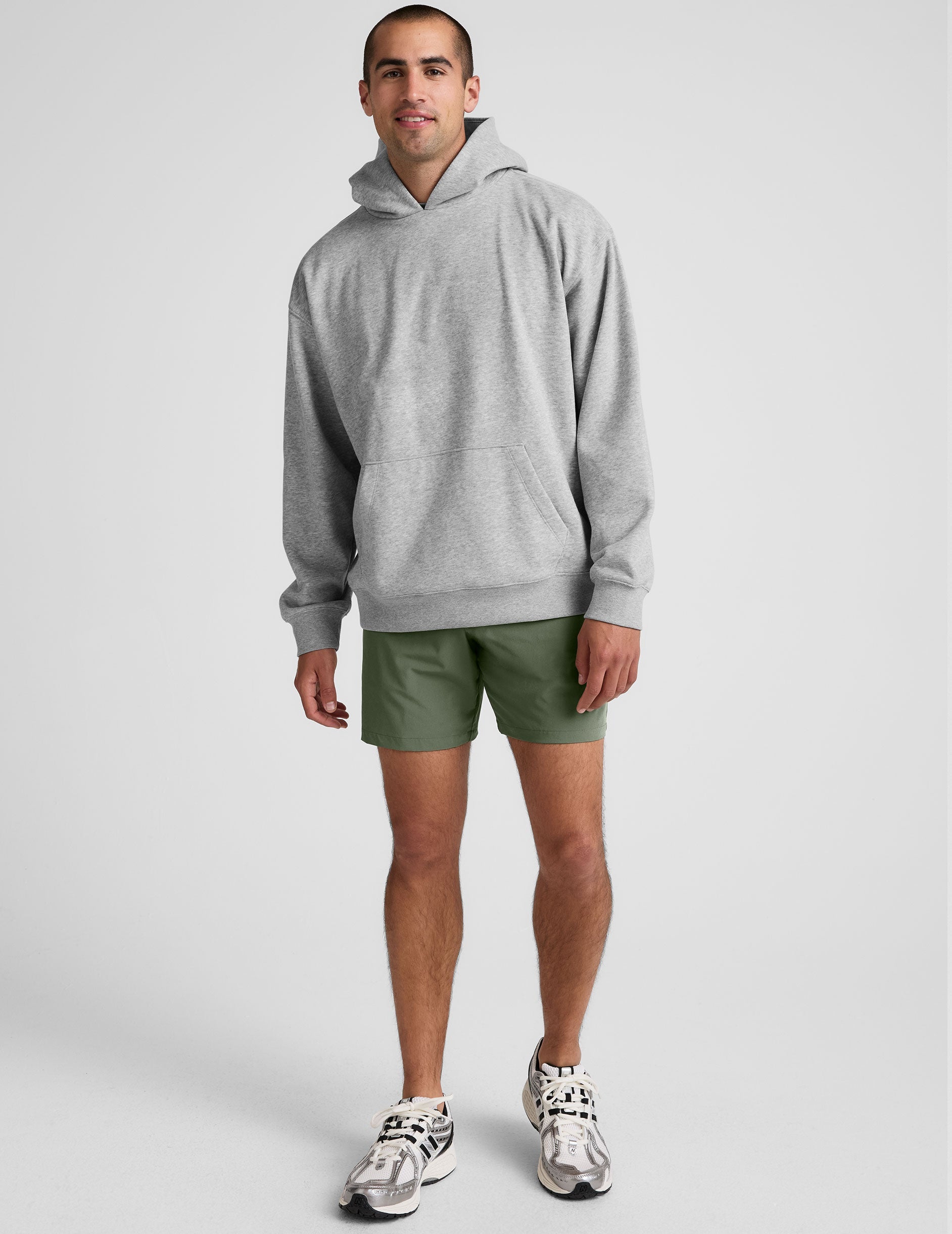 man wearing a gray hoodie and green shorts on a white background.