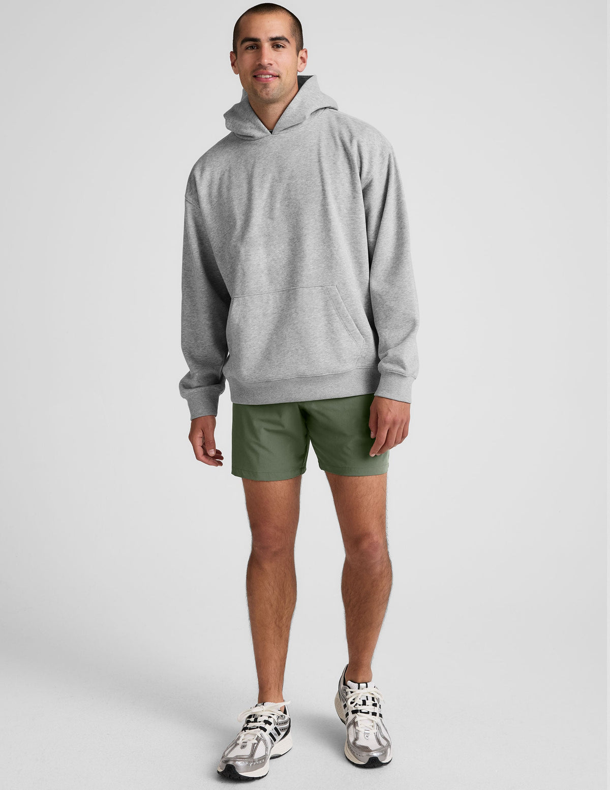 man wearing a gray hoodie and green shorts on a white background.