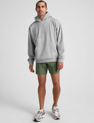 man wearing a gray hoodie and green shorts on a white background.