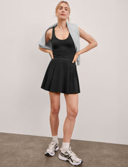 black mini dress in our stretch woven fabric with stitch down front pleats, a scoop front neckline​, open back detail​, bodice in performance stretch fabric​, and skirt side vents for easy pocket access​. 
