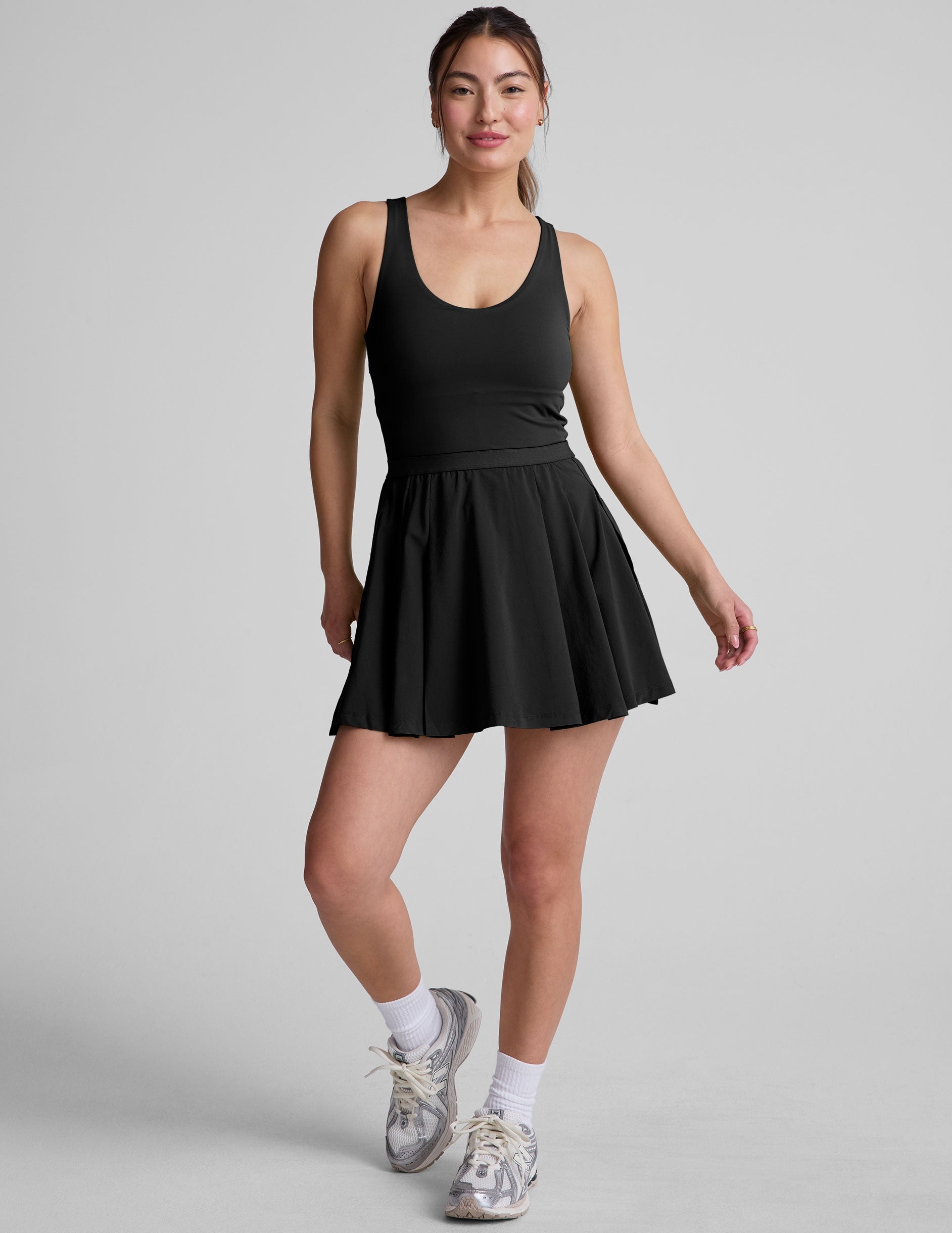 black mini dress in our stretch woven fabric with stitch down front pleats, a scoop front neckline​, open back detail​, bodice in performance stretch fabric​, and skirt side vents for easy pocket access​. 