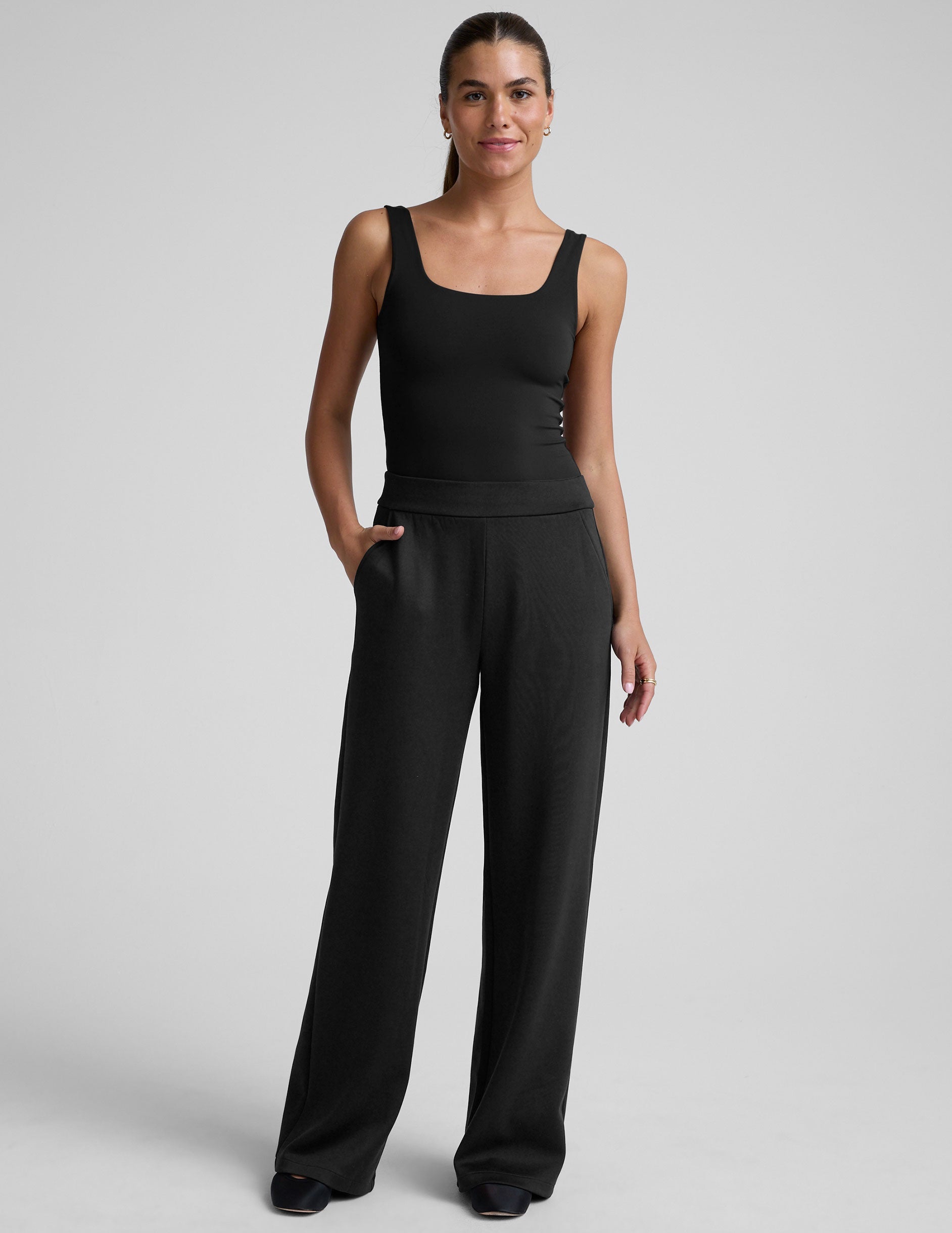 model is wearing a black sleeveless top and black spacer style pants with pockets against a plain background.