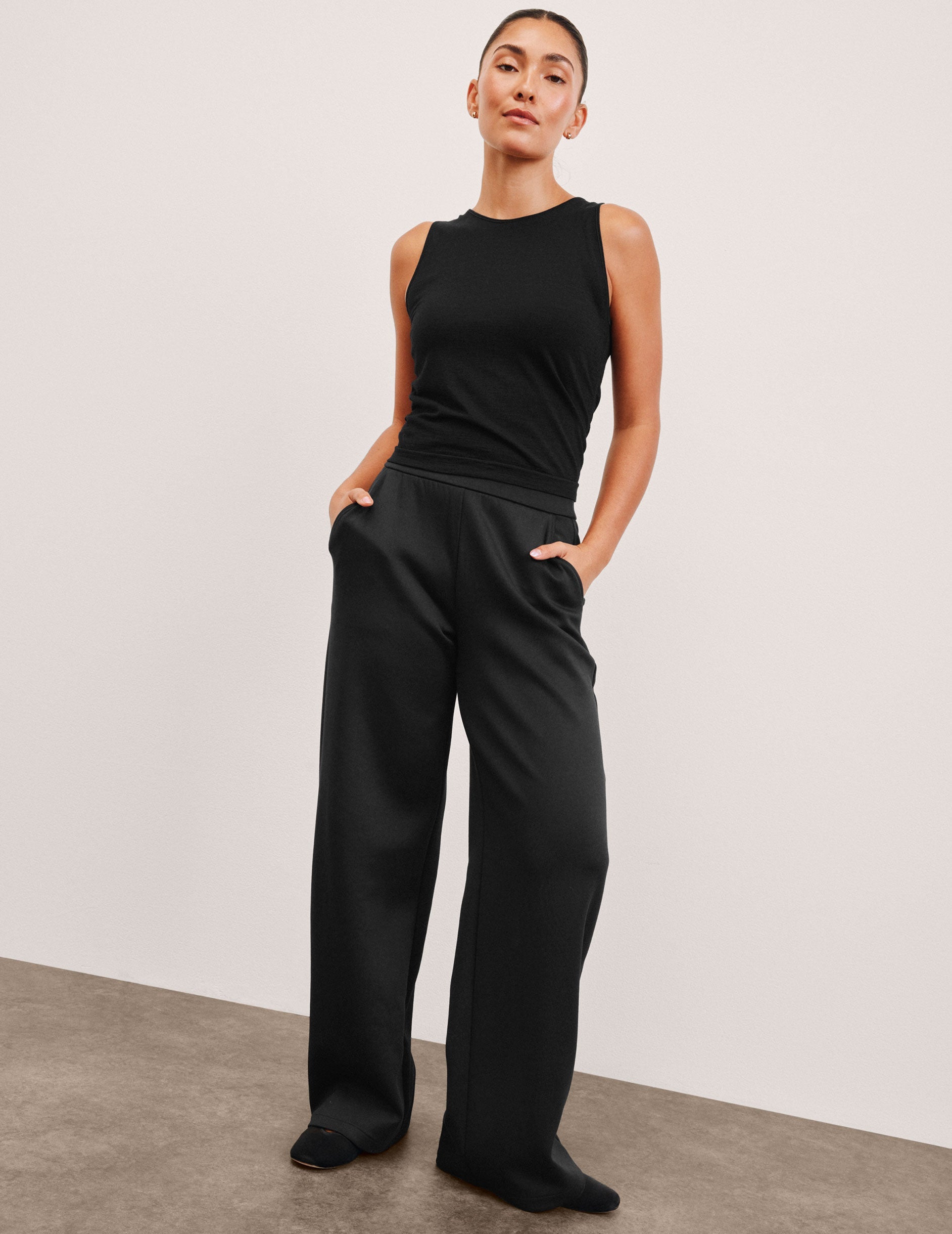 model is wearing a black sleeveless top and black spacer style pants with pockets against a plain background.