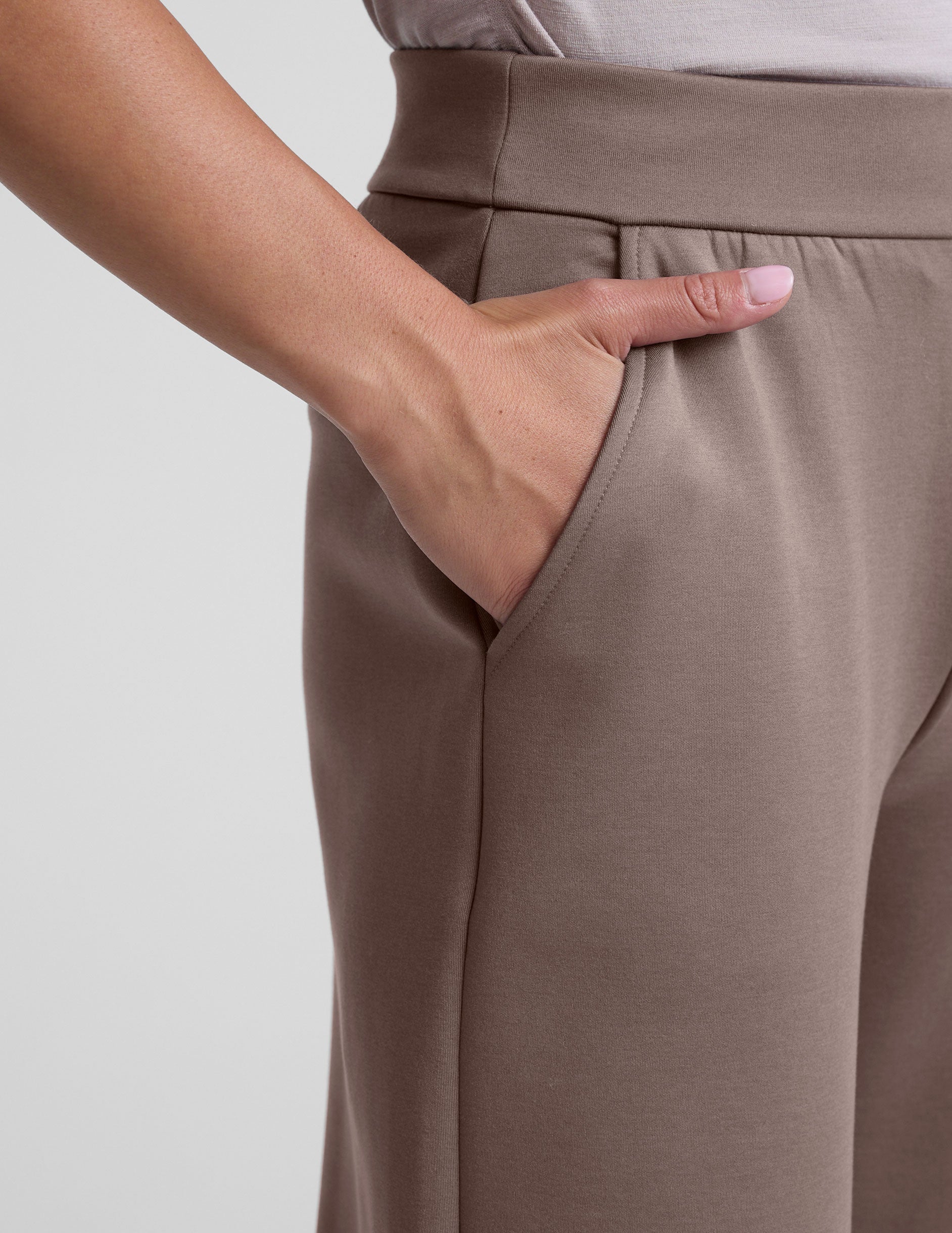 model is wearing brown spacer style pants with pockets against a plain background.