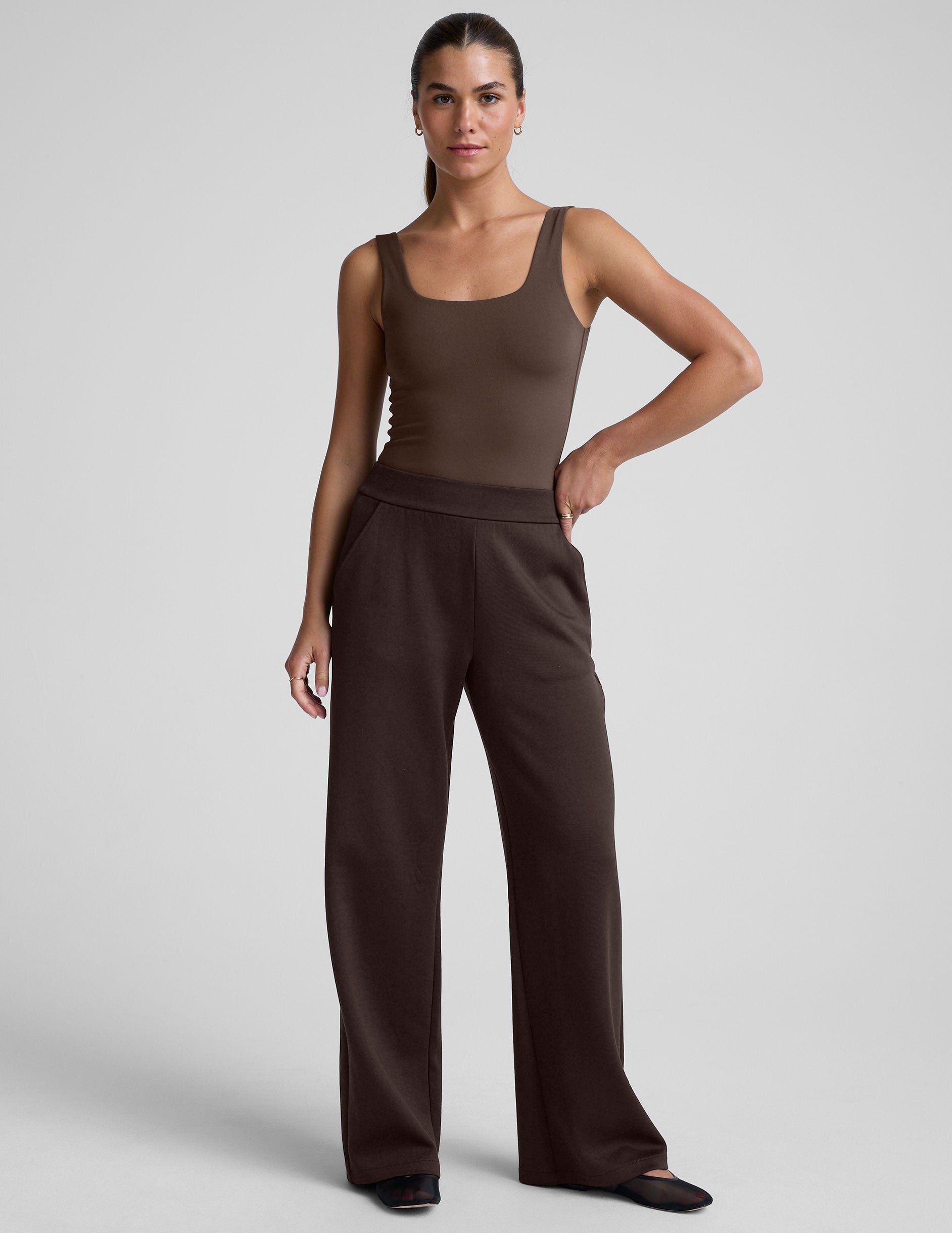 woman wearing brown wide-leg pants against a plain background.