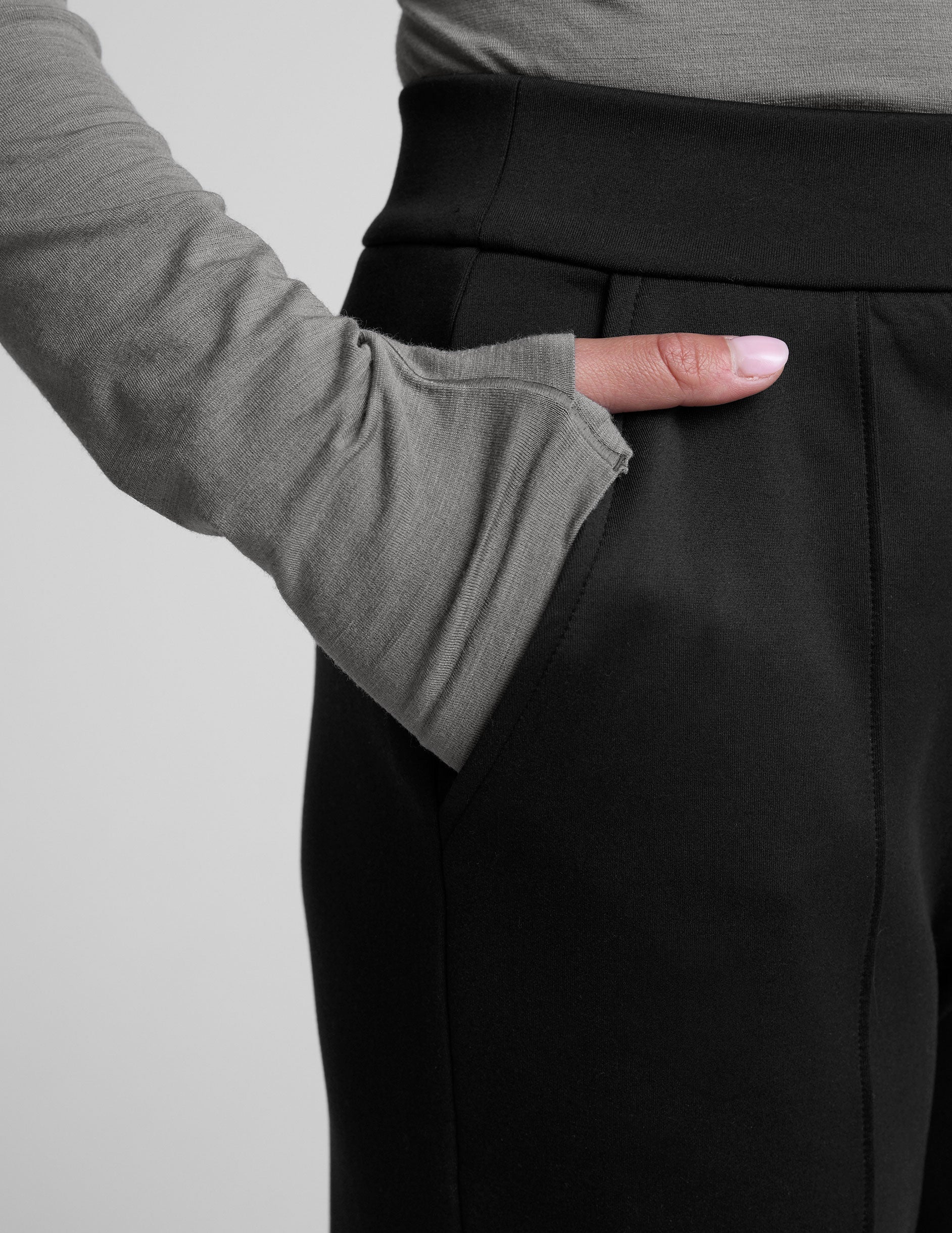 woman wearing a gray turtleneck and black tapered pants on a white background.