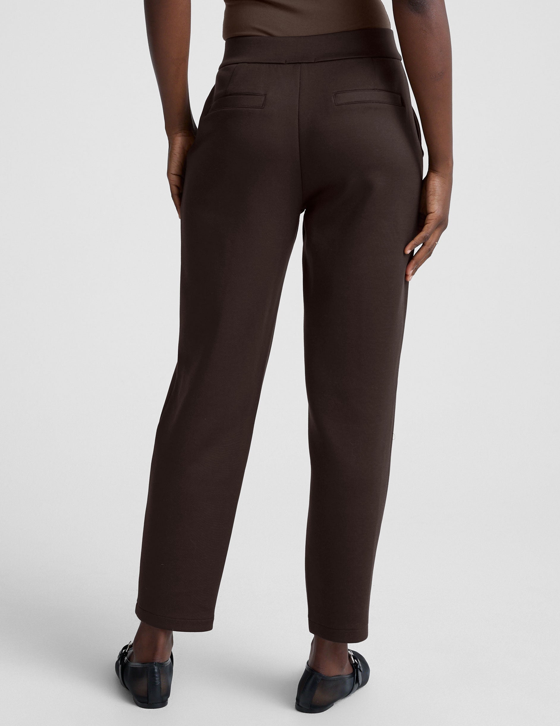 woman wearing brown tapered pants against a plain background.