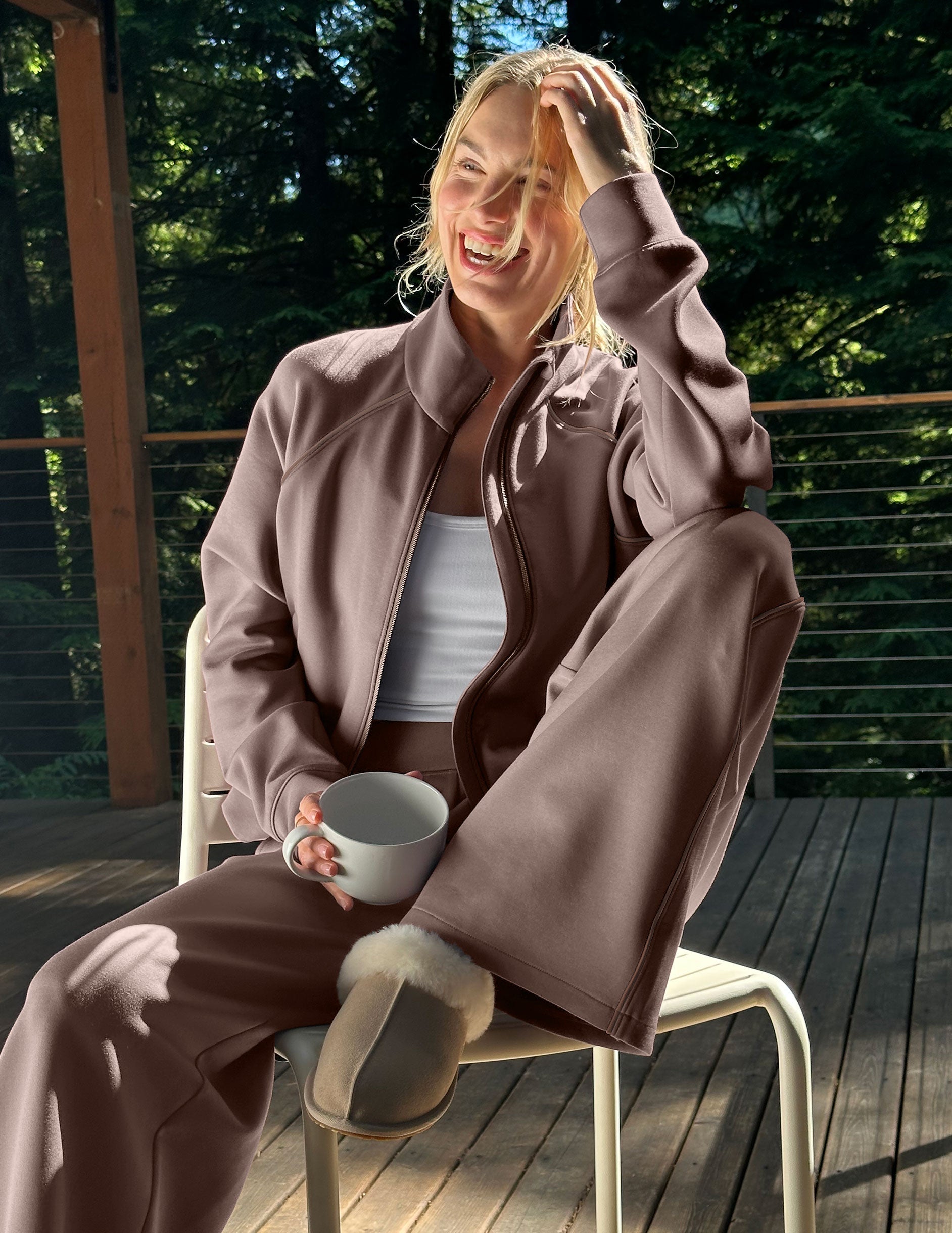 Woman wearing a brown zip-up jacket and pants sitting on a porch.
