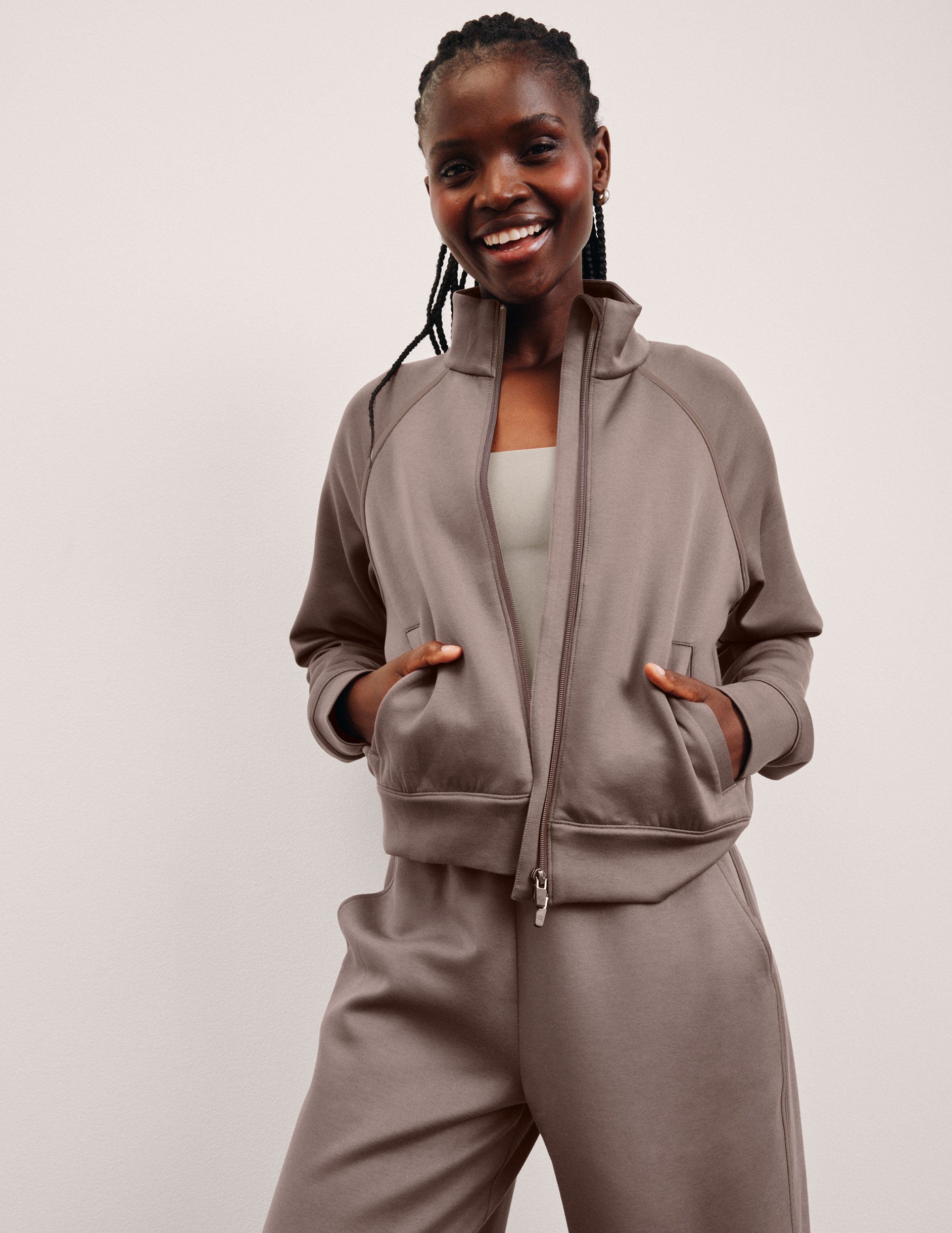 Woman wearing a brown zip-up jacket and pants on a plain background.