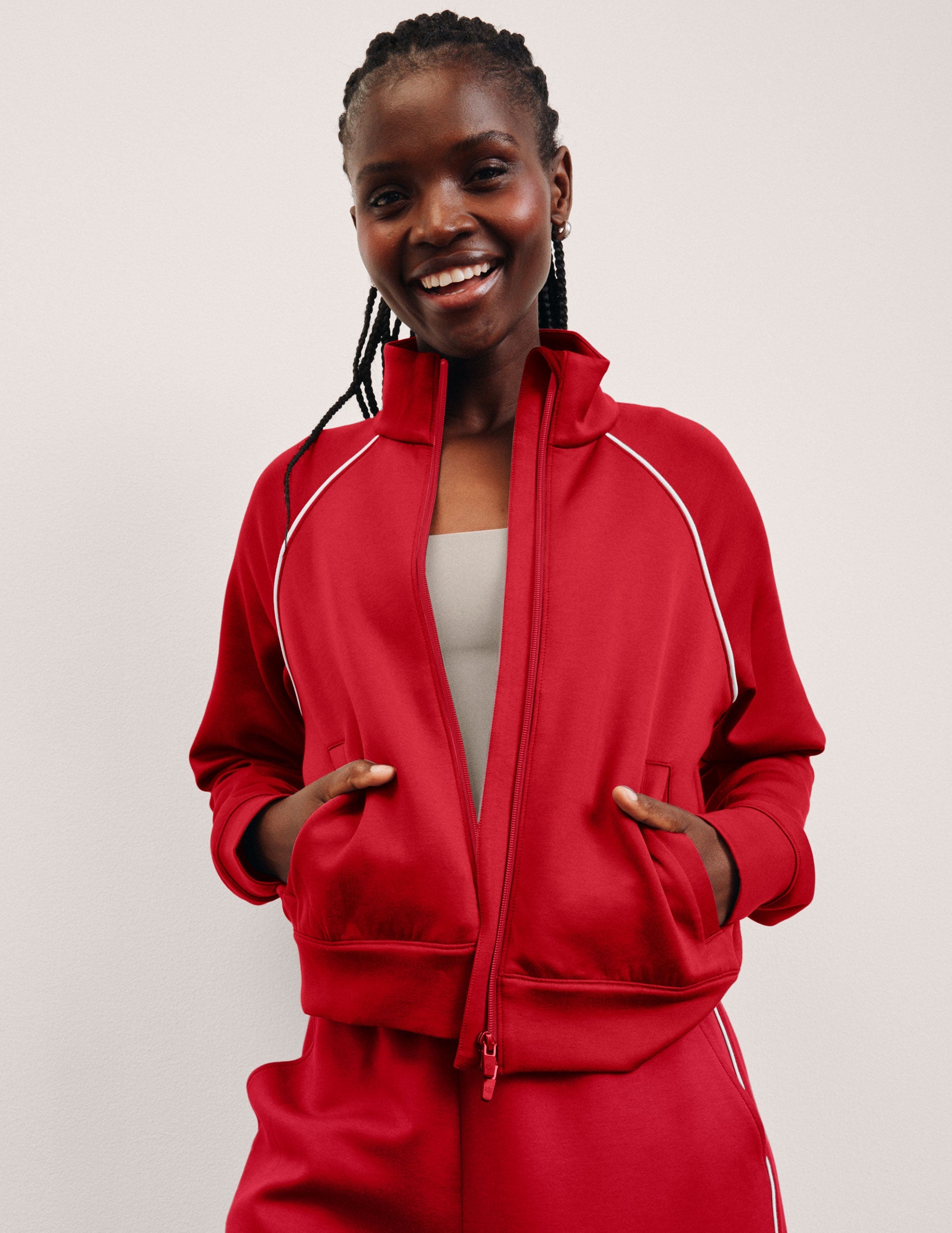 woman wearing a red zip-up jacket with white piping against a plain background.