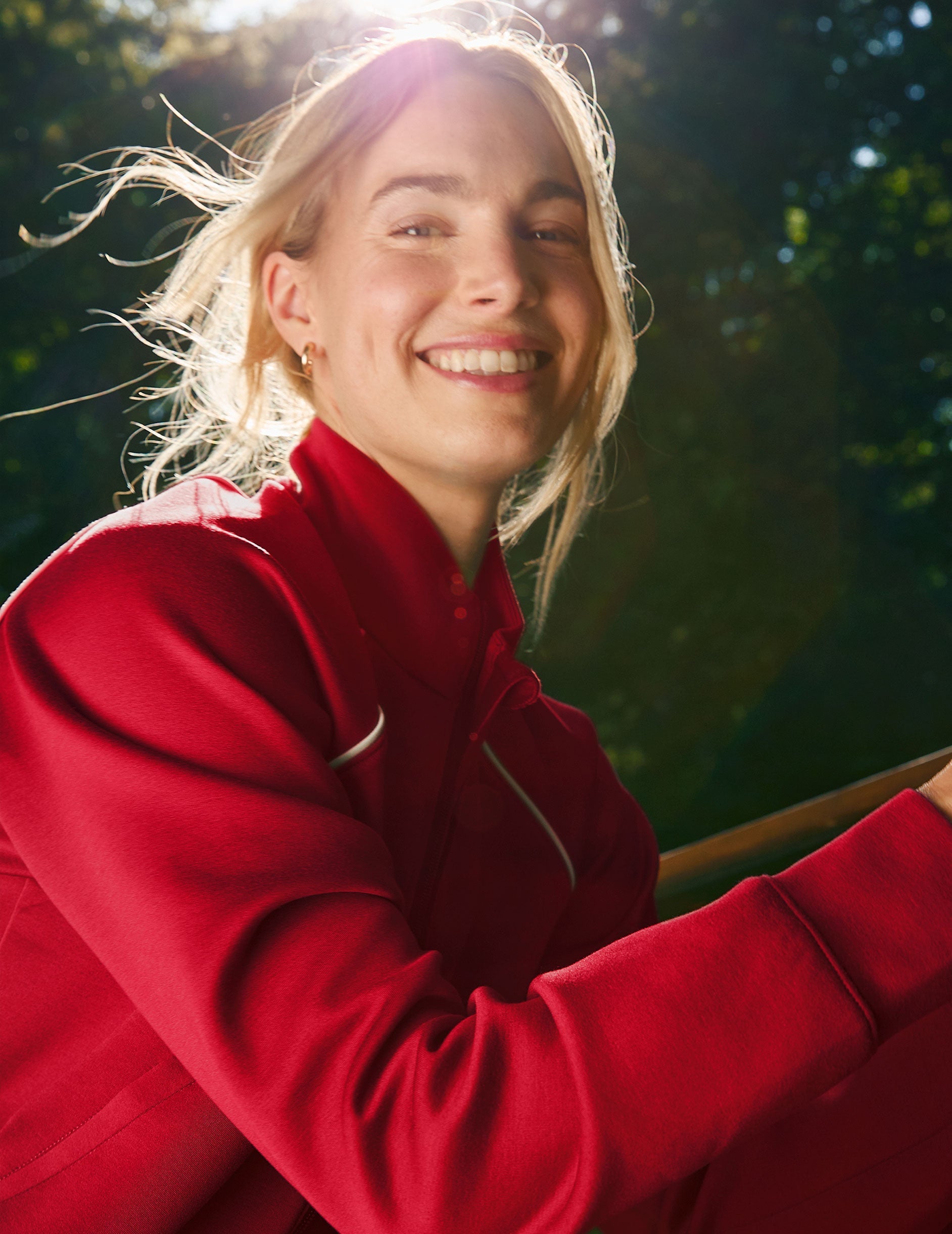 woman wearing a red zip-up jacket with white piping against a nature background.