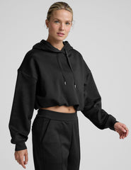 woman wearing a black cropped hoodie and pants on a plain background.