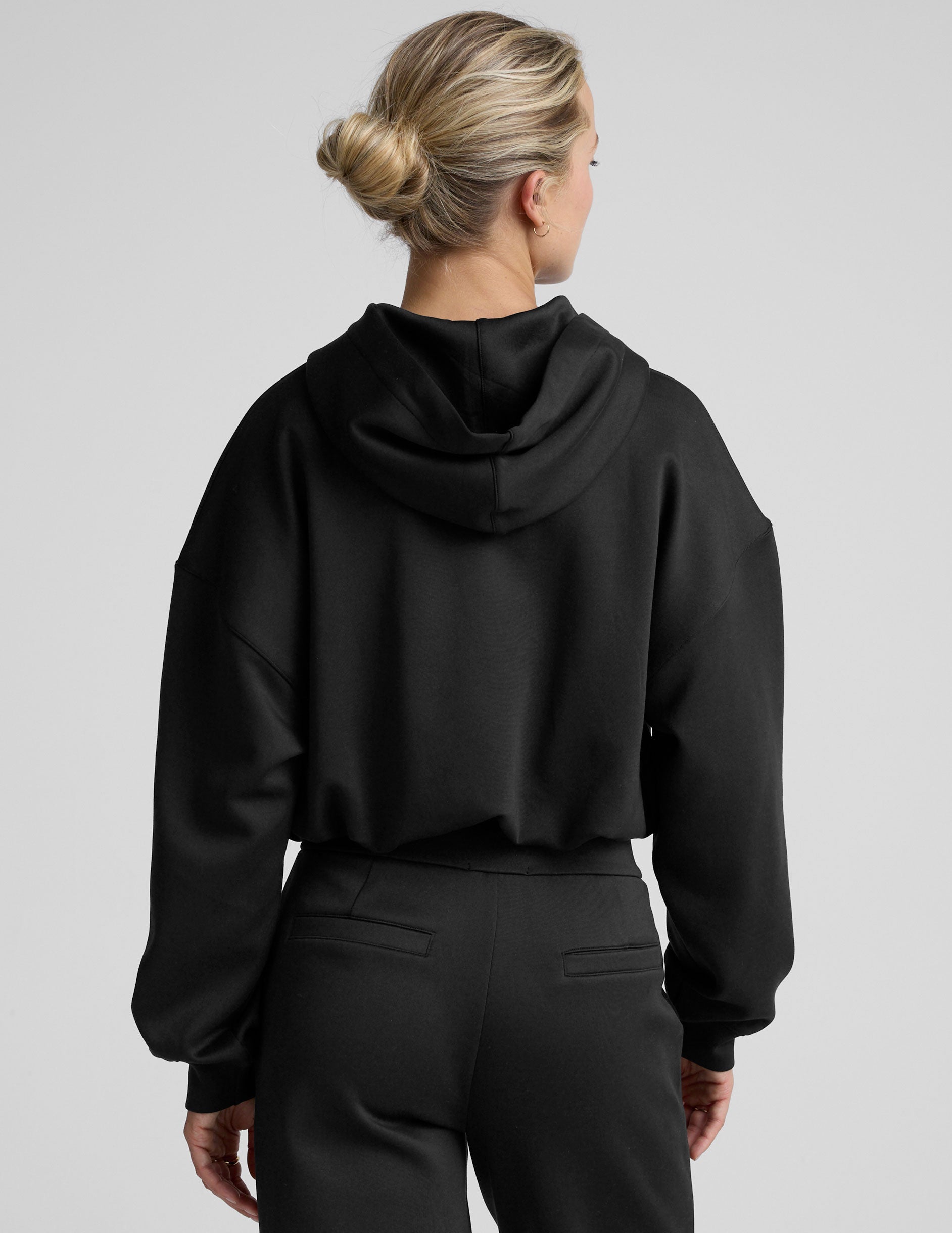 woman wearing a black cropped hoodie and pants on a plain background.