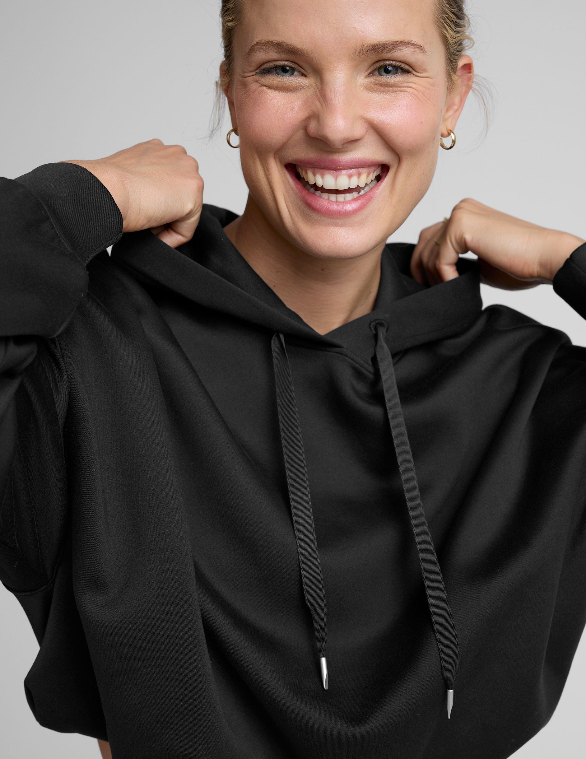 woman wearing a black cropped hoodie and pants on a plain background.