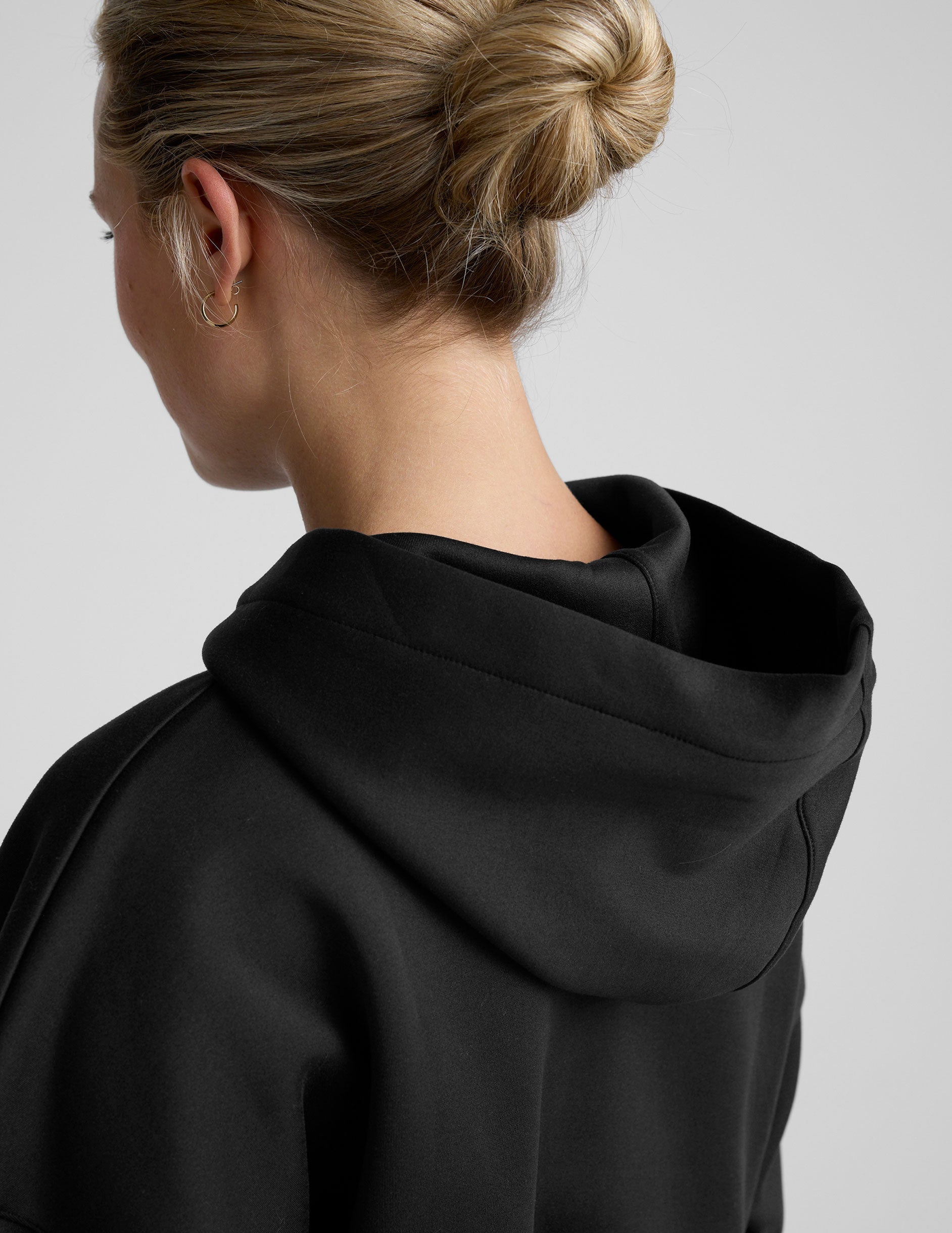 woman wearing a black cropped hoodie and pants on a plain background.