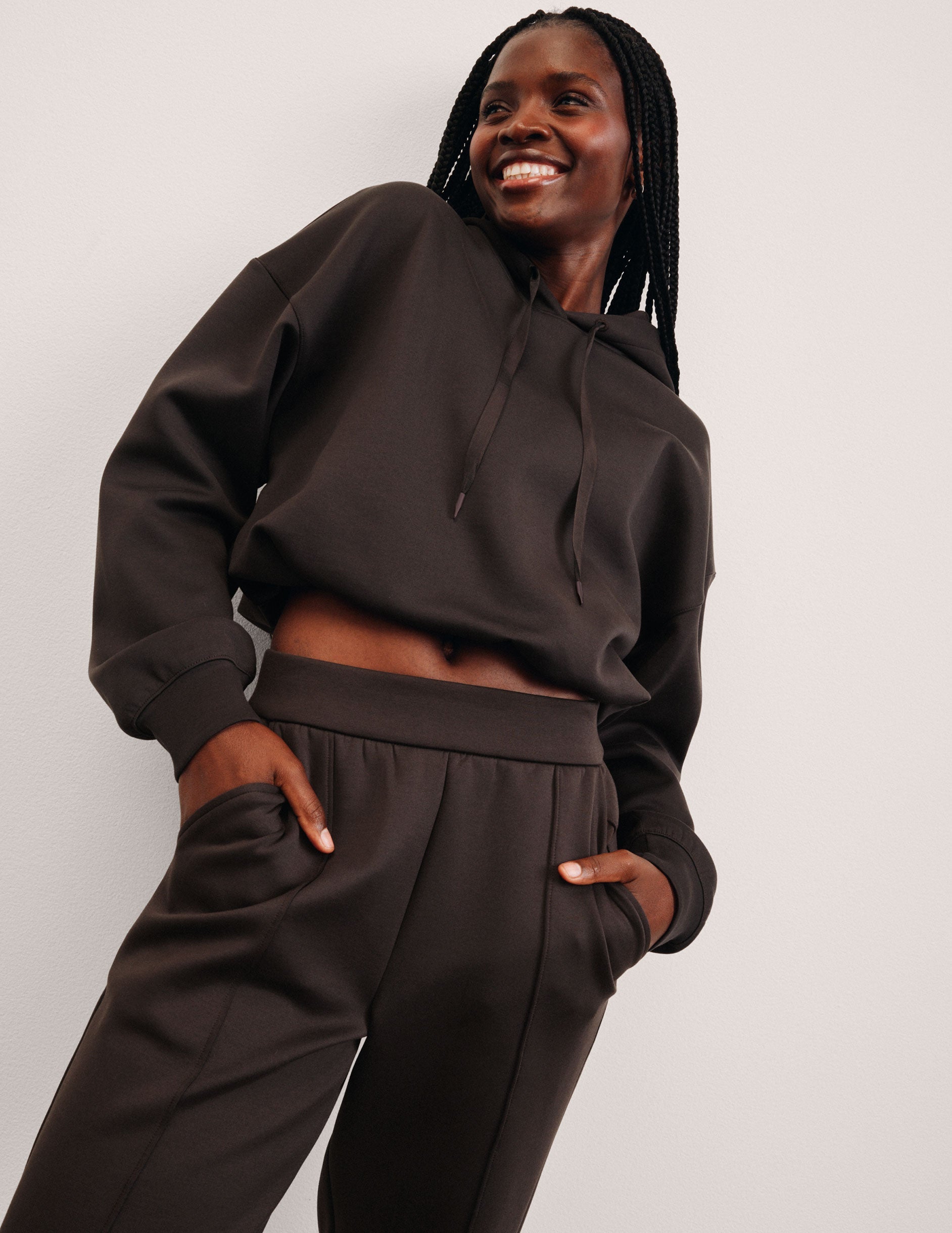 woman wearing a brown cropped hoodie and pants against a plain background.