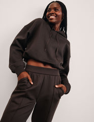 woman wearing a brown cropped hoodie and pants against a plain background.