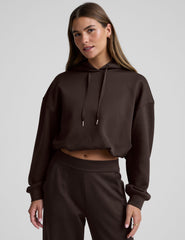 woman wearing a brown cropped hoodie and pants against a plain background.