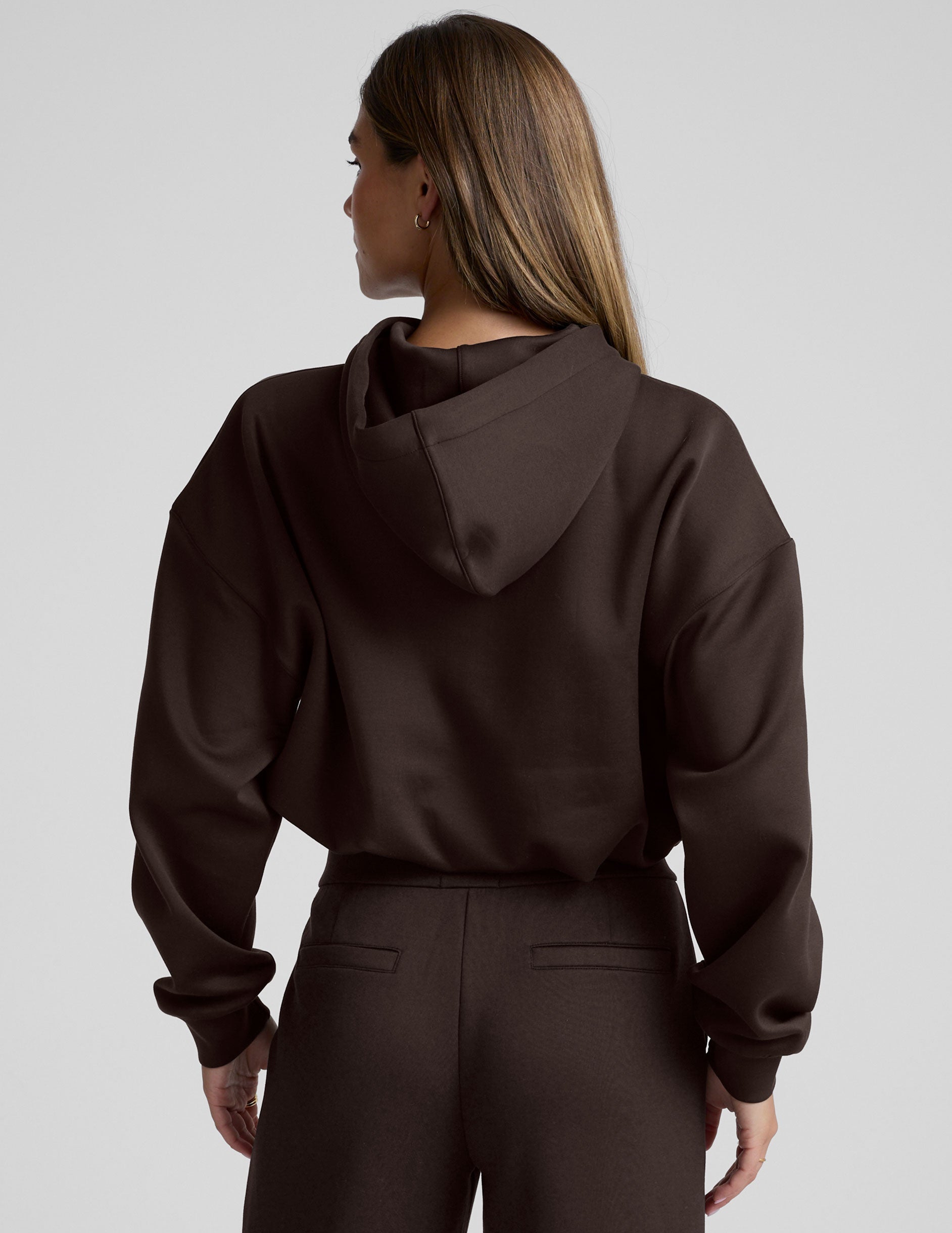 woman wearing a brown cropped hoodie and pants against a plain background.