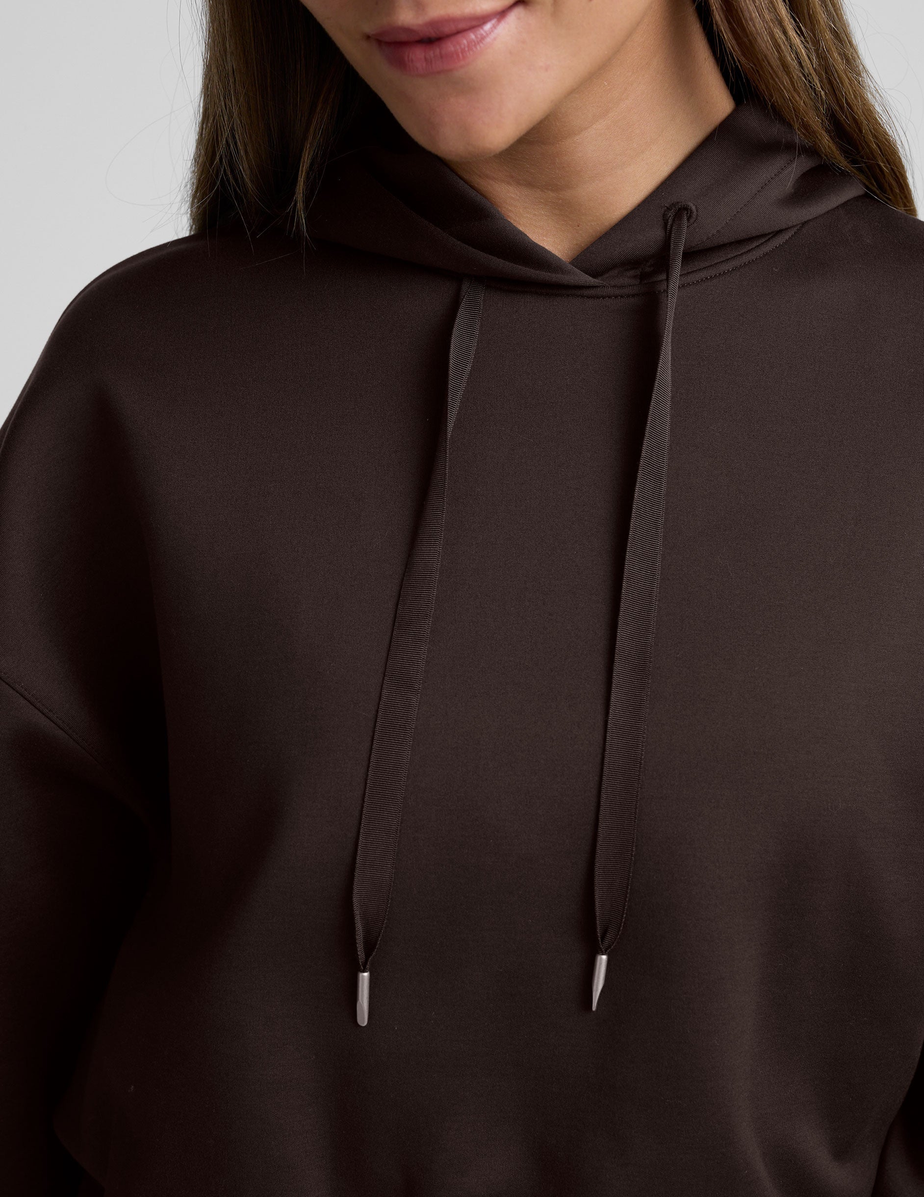 woman wearing a brown cropped hoodie and pants against a plain background.