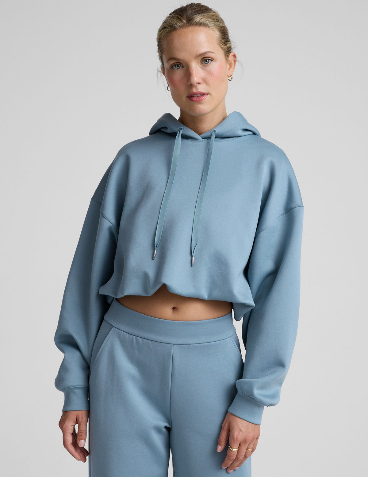woman wearing a light blue hoodie and matching pants on a plain background.