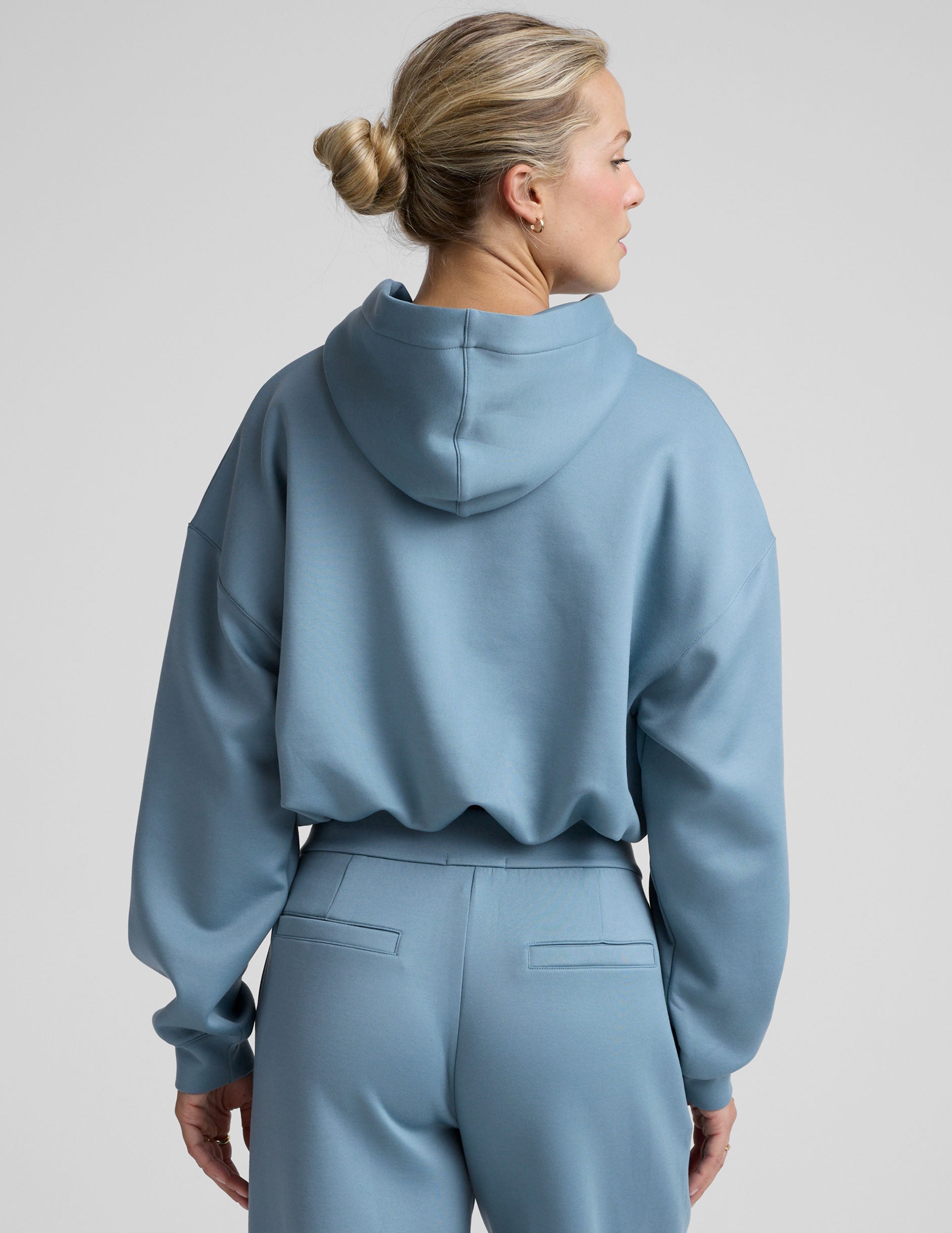 woman wearing a light blue hoodie and matching pants on a plain background.