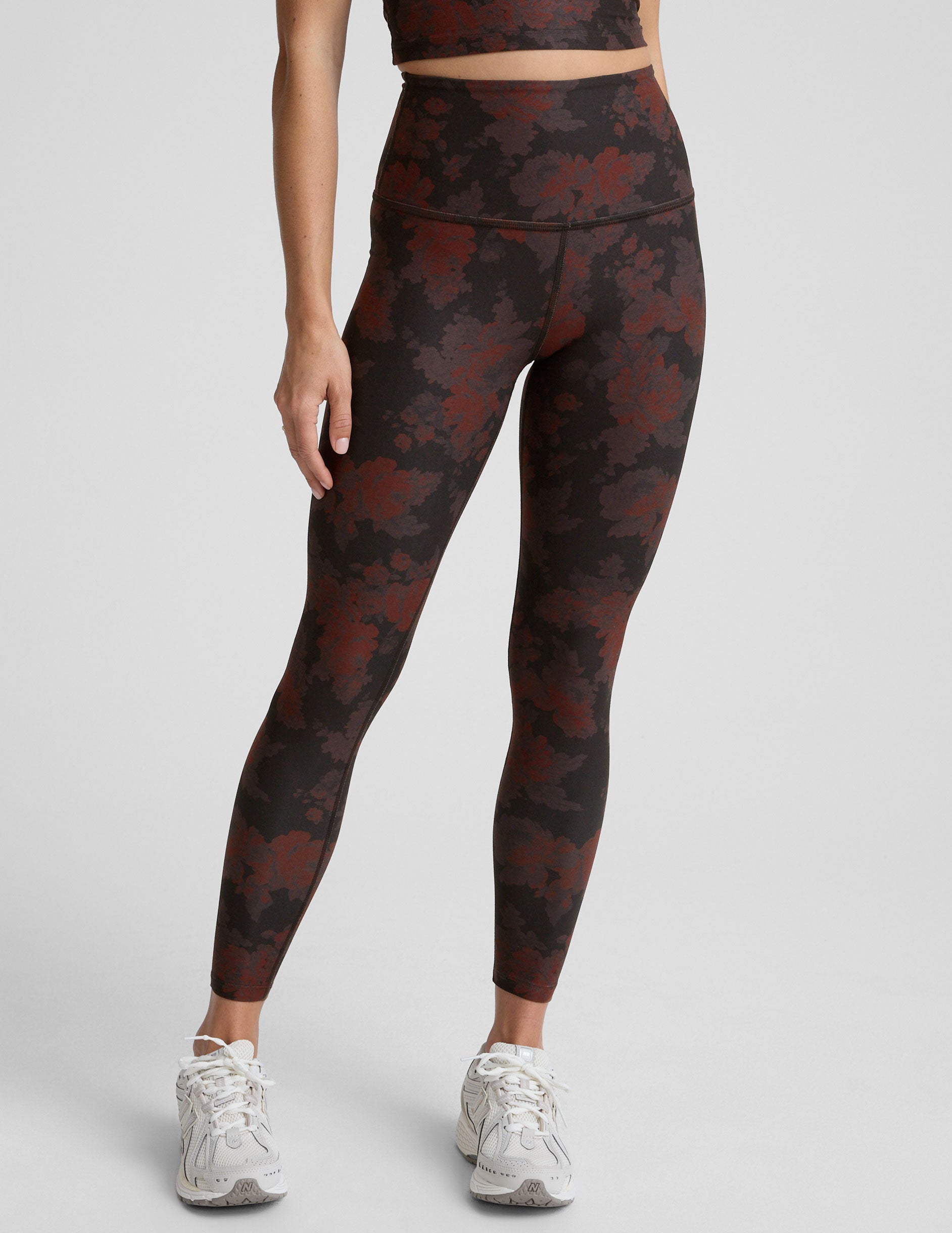 person wearing red and brown printed leggings on a light gray background.
