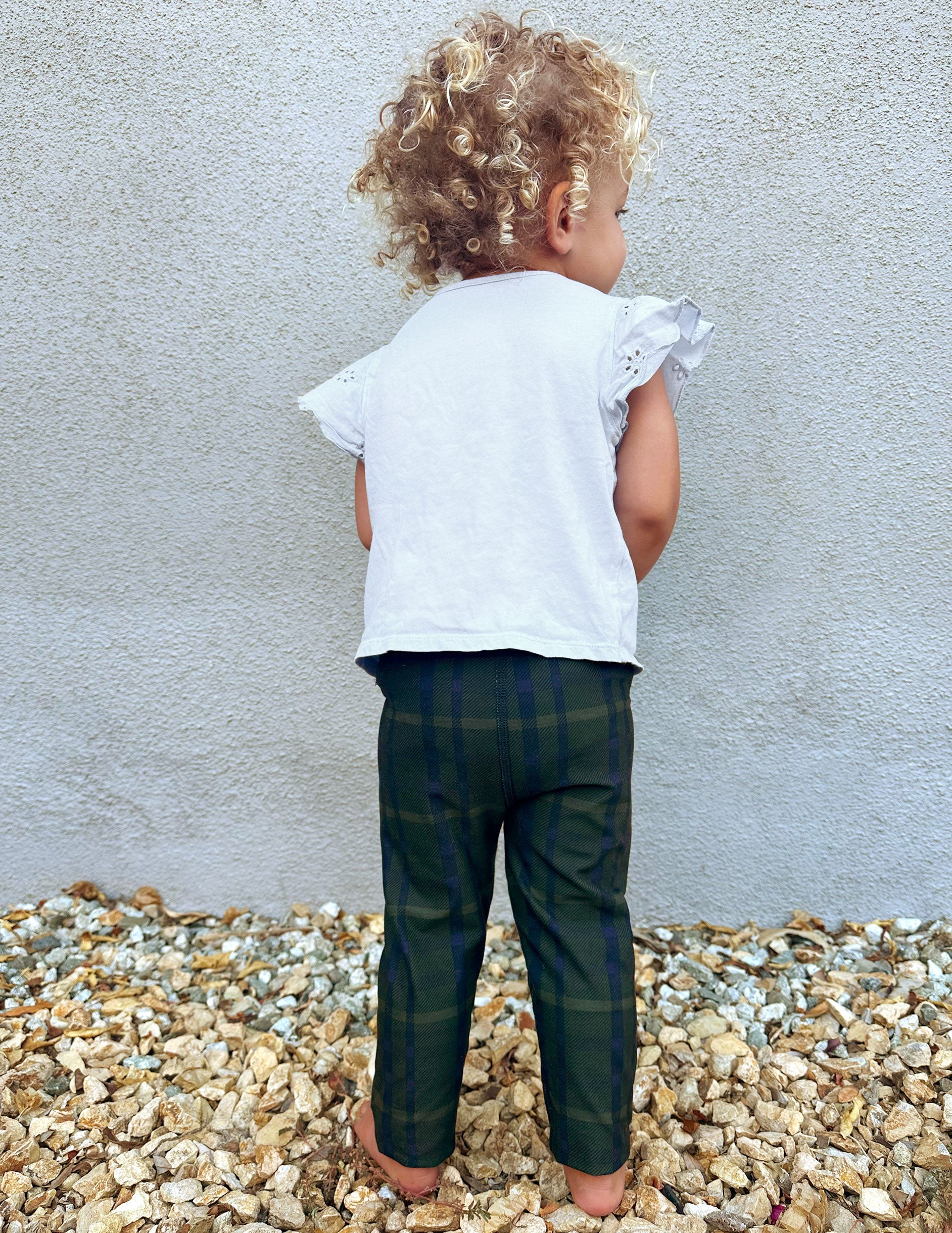 model wearing a white top and green plaid pants standing on gravel against a light gray wall.