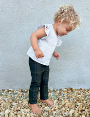 model wearing a white top and green plaid pants standing on gravel against a light gray wall.