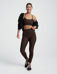 Woman wearing a brown leopard printed  bra and leggings on a plain background.