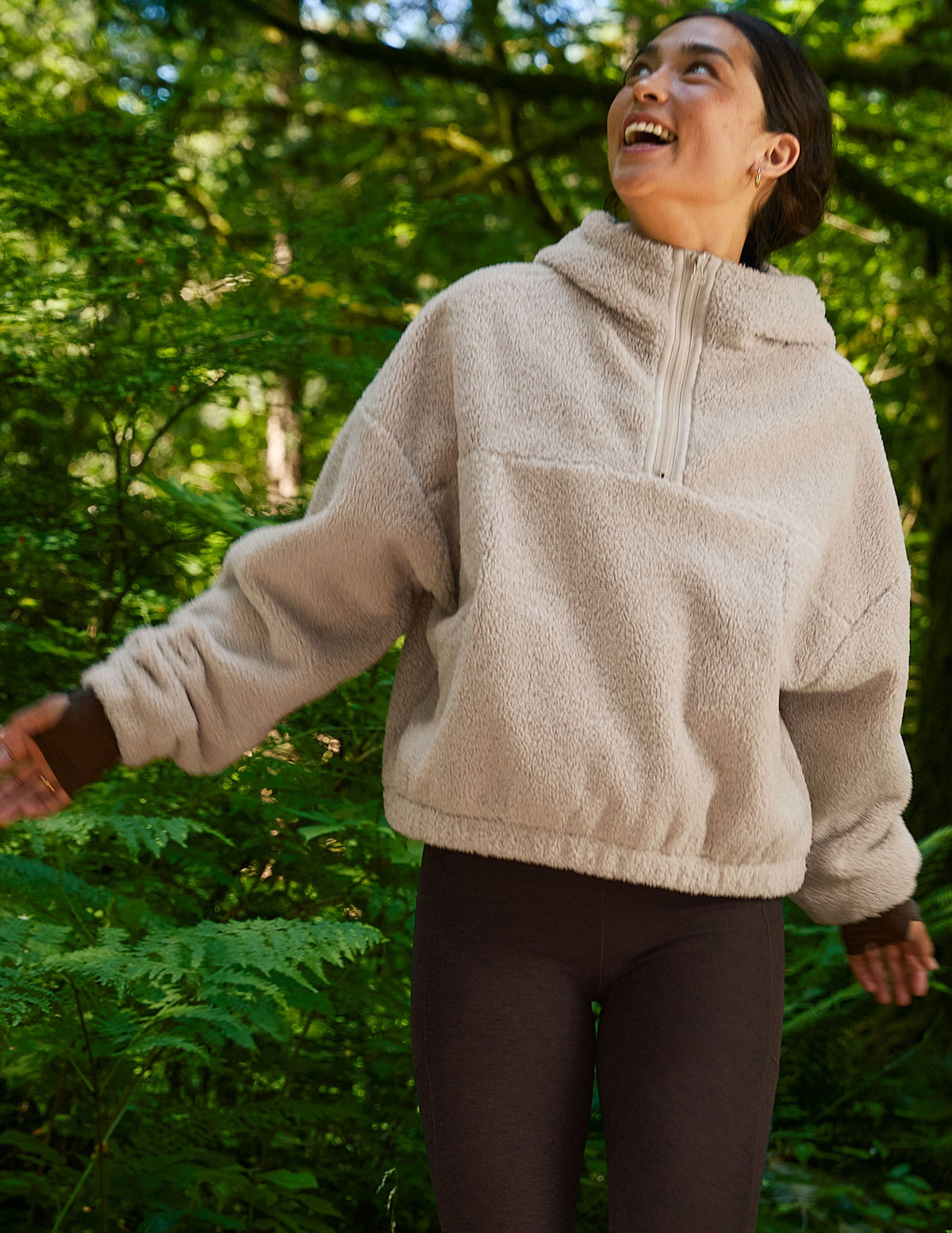 model wearing a beige fleece pullover in a forest setting.