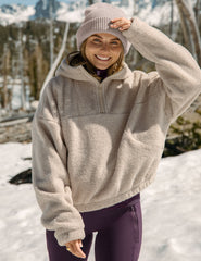 model wearing a beige fleece quarter zip pullover and purple pants in a snowy landscape.