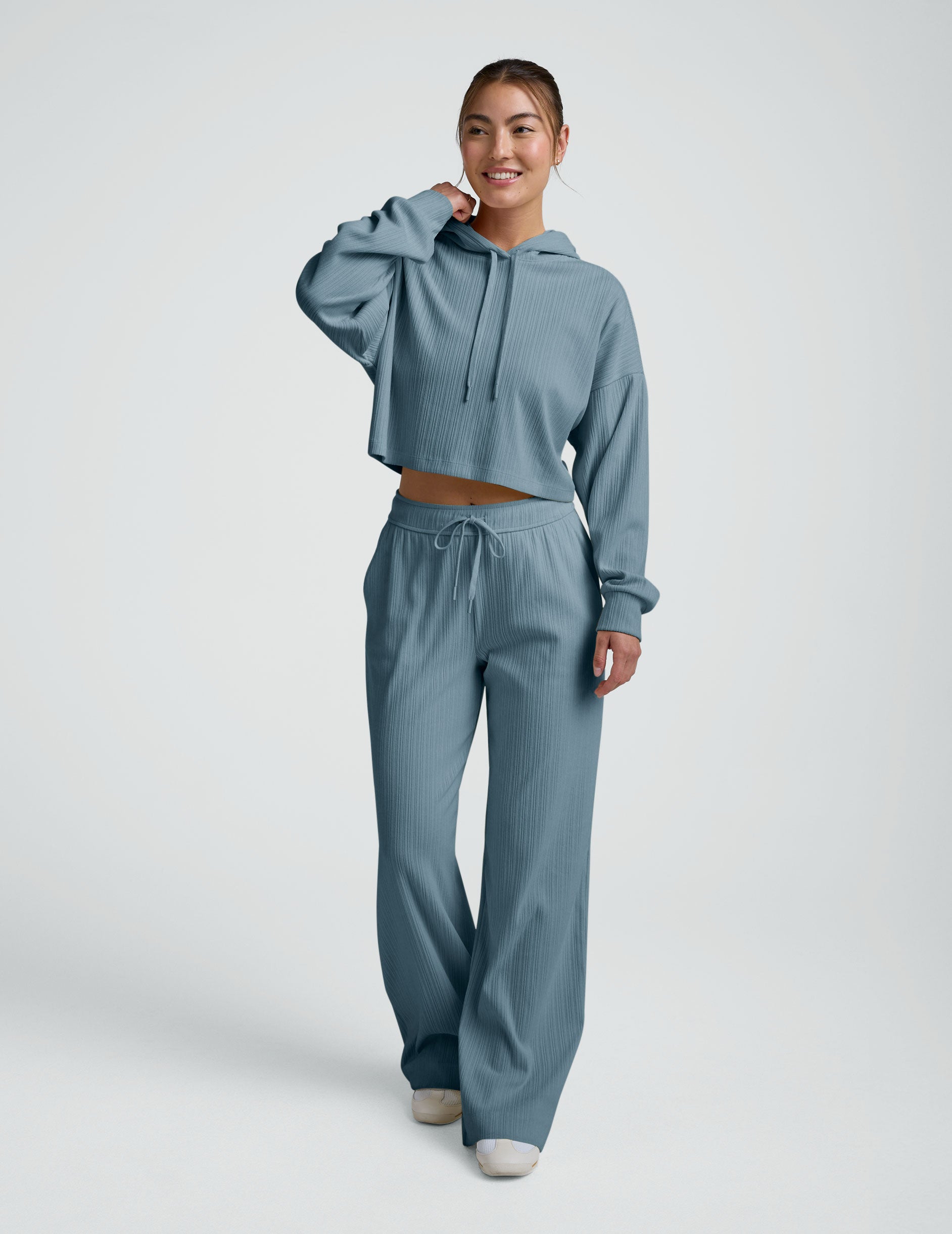 woman wearing a blue ribbed cropped hoodie and pants on a plain background.