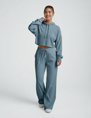 woman wearing a blue ribbed cropped hoodie and pants on a plain background.