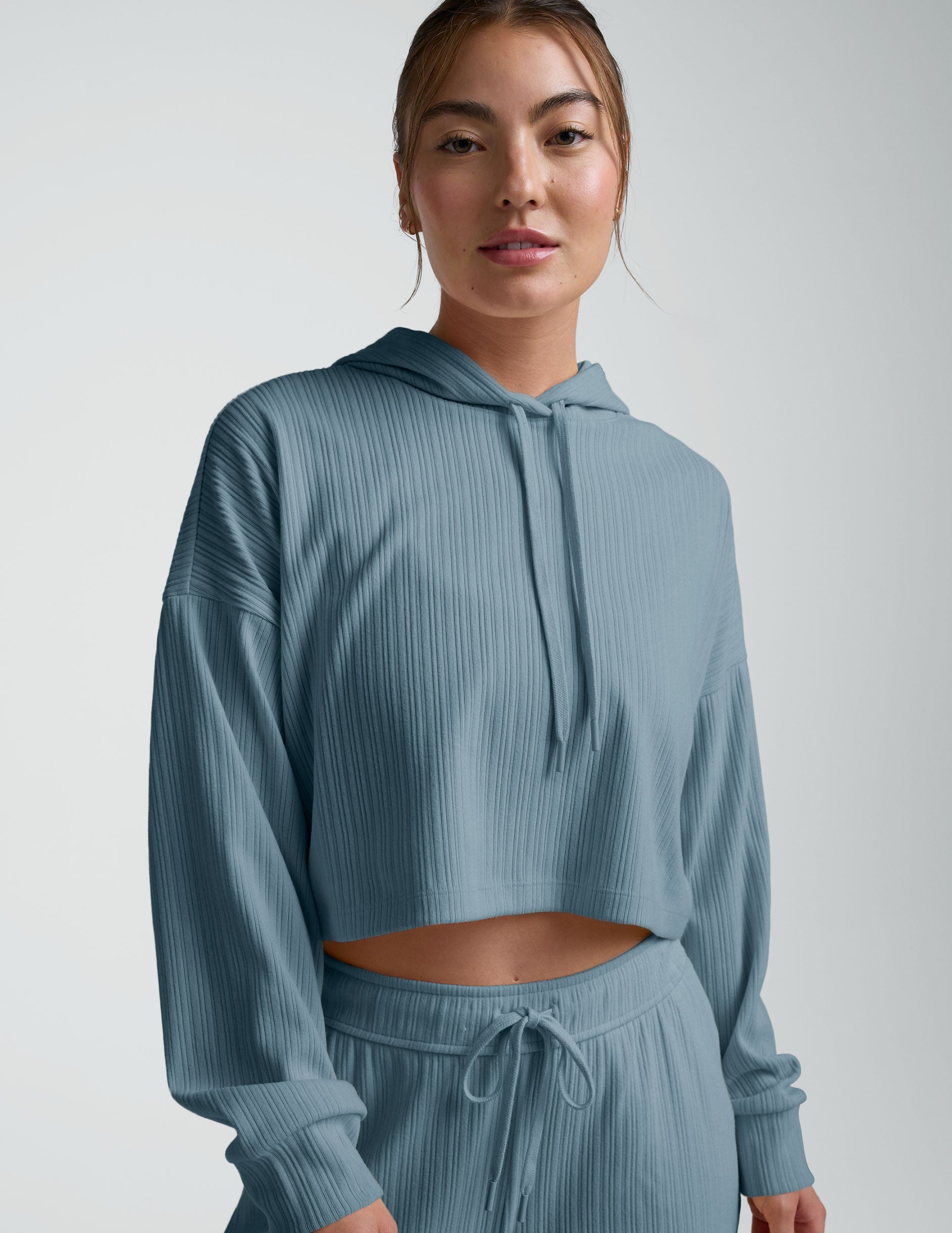 woman wearing a blue ribbed cropped hoodie and pants on a plain background.