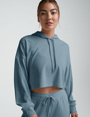 woman wearing a blue ribbed cropped hoodie and pants on a plain background.