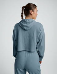 woman wearing a blue ribbed cropped hoodie and pants on a plain background.