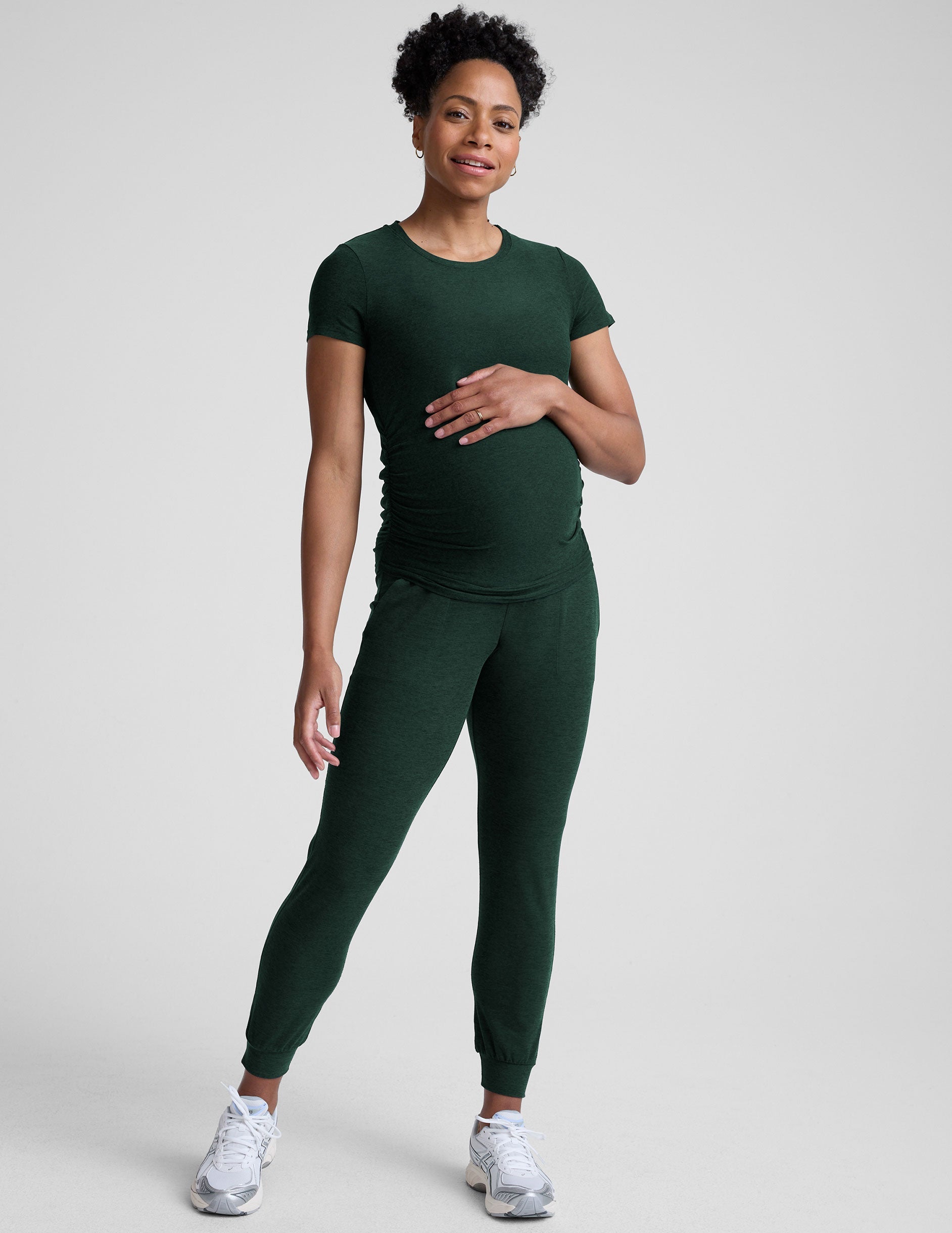 model wearing a green maternity t-shirt and green maternity midi length joggers  on a plain background.