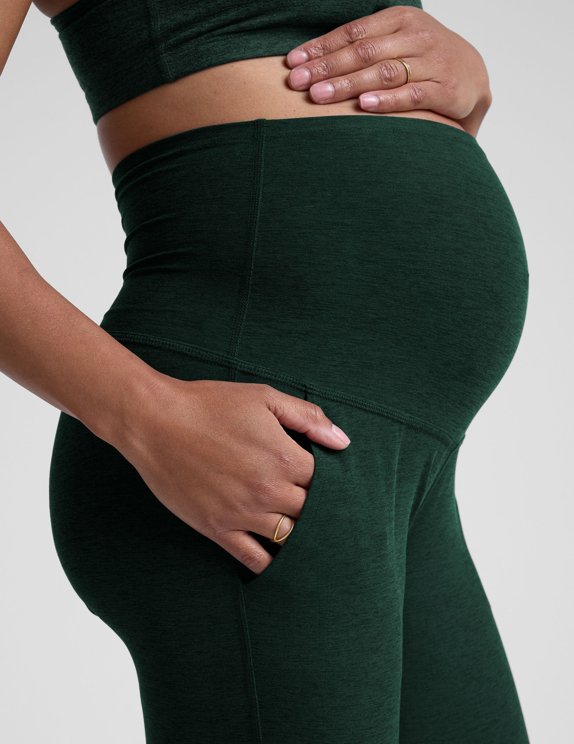 model wearing green maternity midi length joggers with pockets on a plain background.