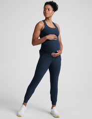 pregnant woman wearing a navy blue racerback maternity tank and maternity joggers with pockets on a plain background.