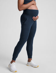pregnant woman wearing navy blue maternity joggers with pockets on a plain background.