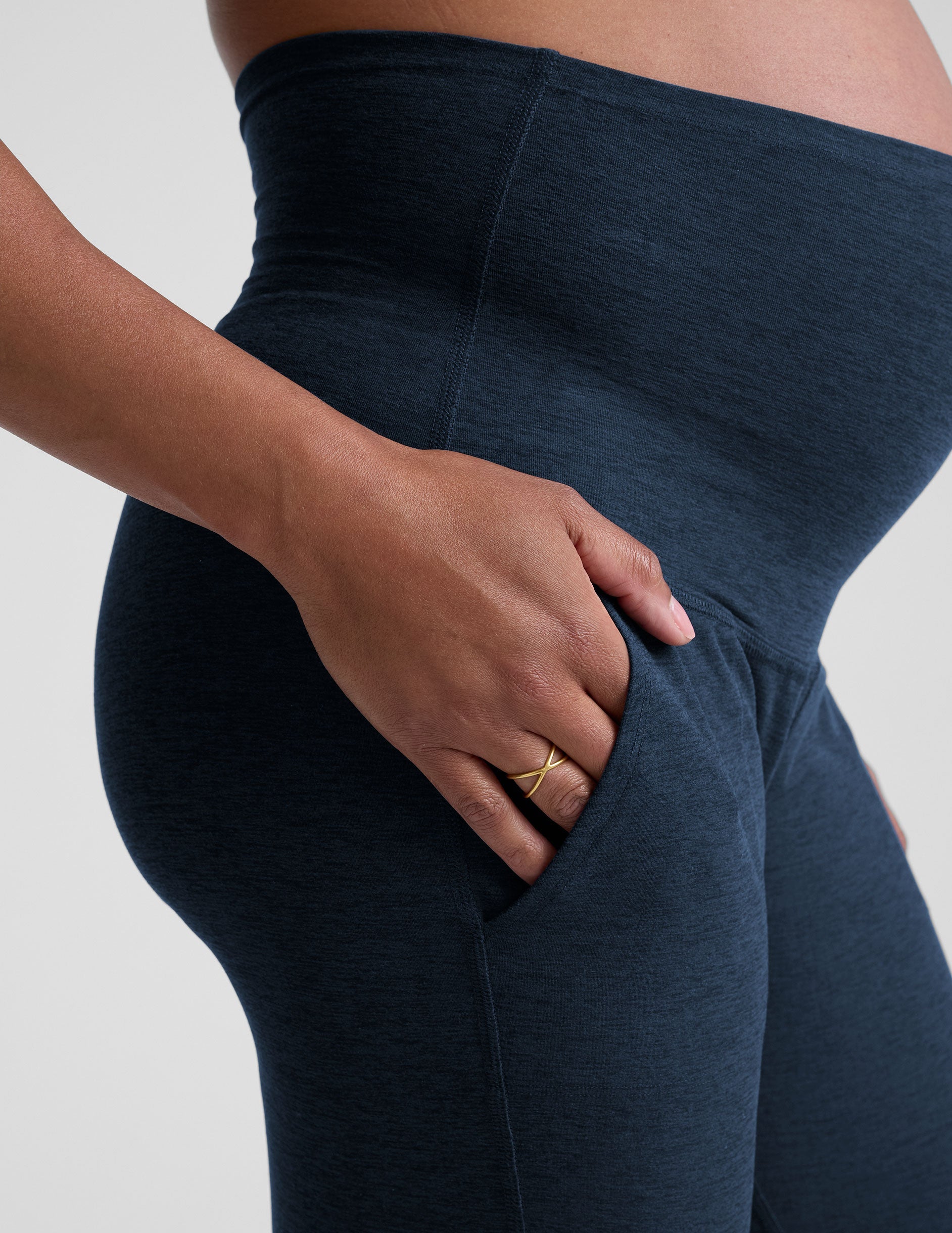 pregnant woman wearing navy blue maternity joggers with pockets on a plain background.