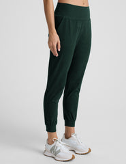 person wearing dark green jogger pants and white sneakers on a plain background.