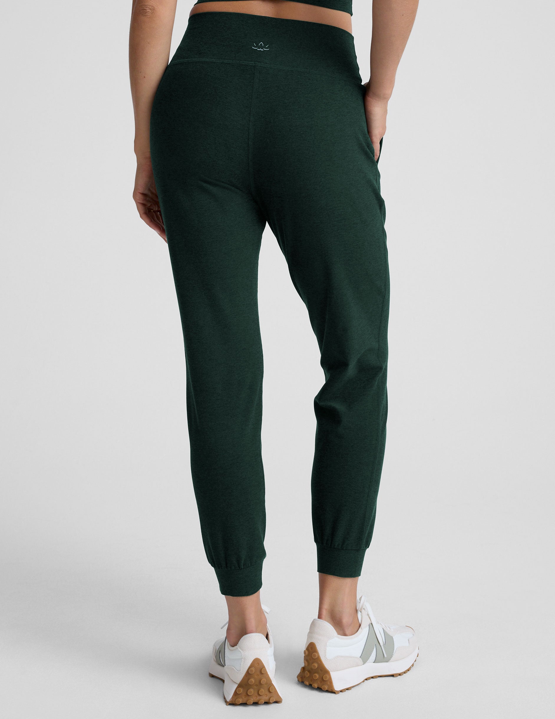 person wearing dark green jogger pants and white sneakers on a plain background.