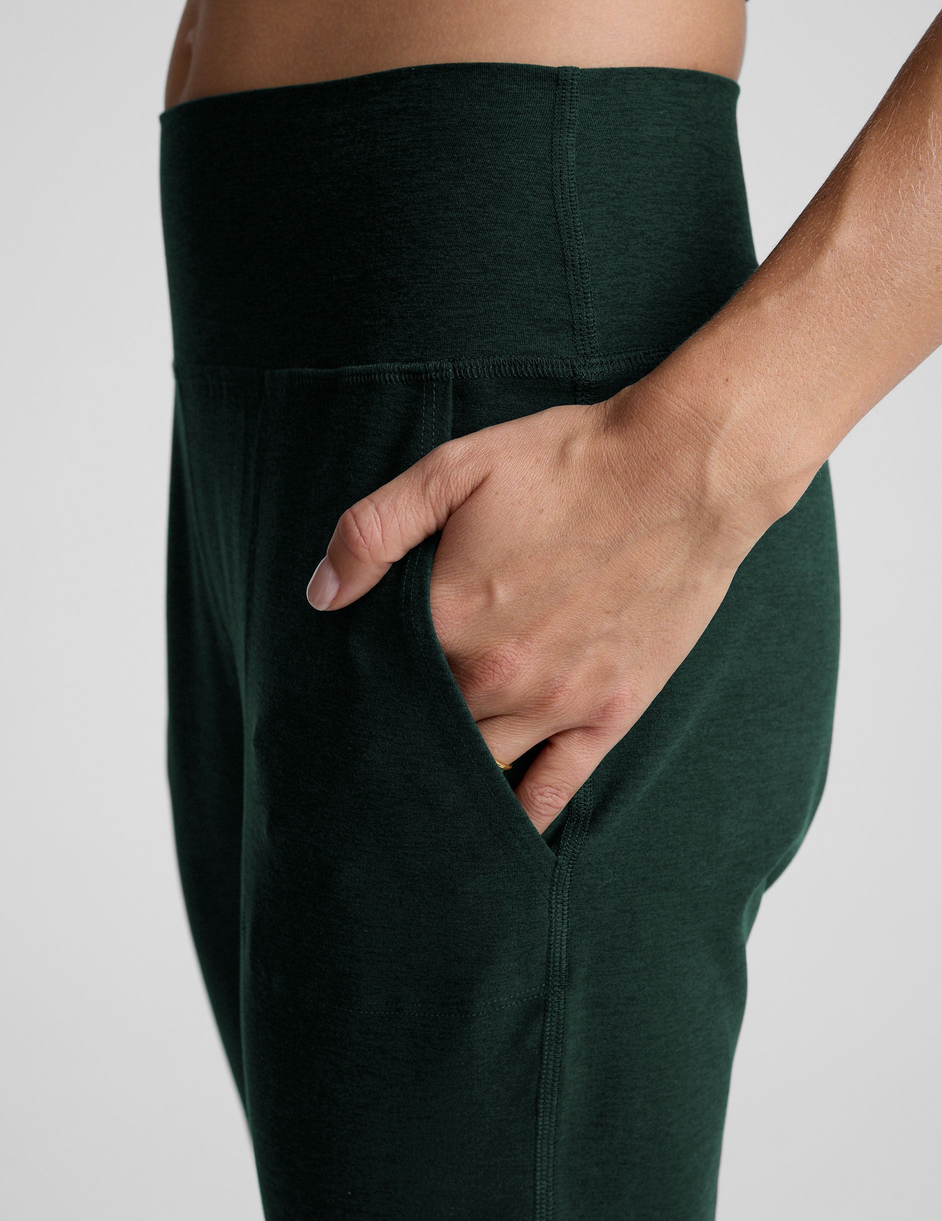 person wearing dark green jogger pants and white sneakers on a plain background.