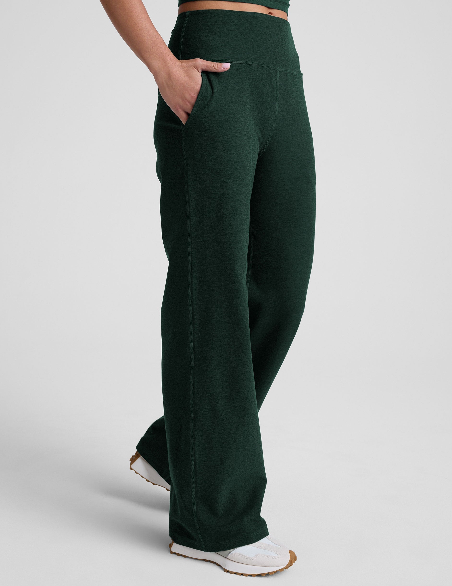 model wearing dark green high-waisted wide leg pants with pockets on a plain background.