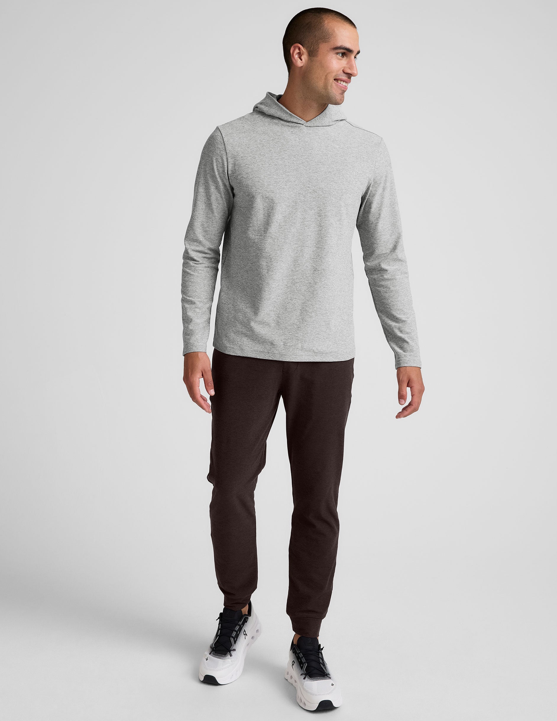 male model wearing a grey hoodie and brown men's sweatpants with zipper pockets on a plain background.