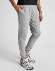 man wearing a black t-shirt and gray sweatpants on a plain background.